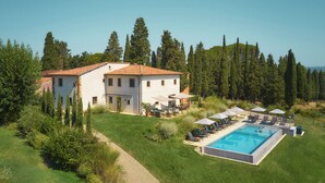 A large house with a swimming pool, surrounded by greenery and trees.