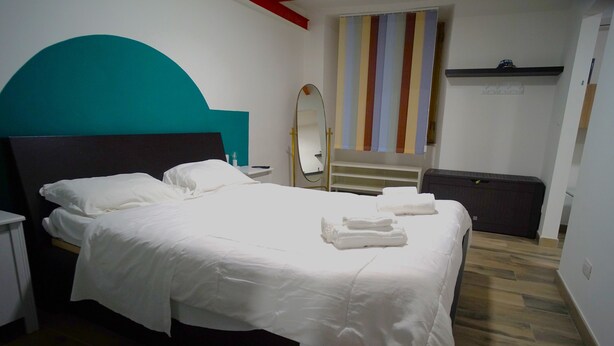 A neatly made bed with white linens, a bedside table, a mirror, and a striped curtain. - Apartment Lallarella 17: historic center of Naples (Napoli)