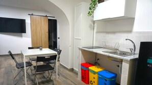 A compact kitchen with a sink, cabinets, and a dining area with chairs. There are colorful trash bins and a plant above the sink. - Apartment Lallarella 17: historic center of Naples (Napoli)