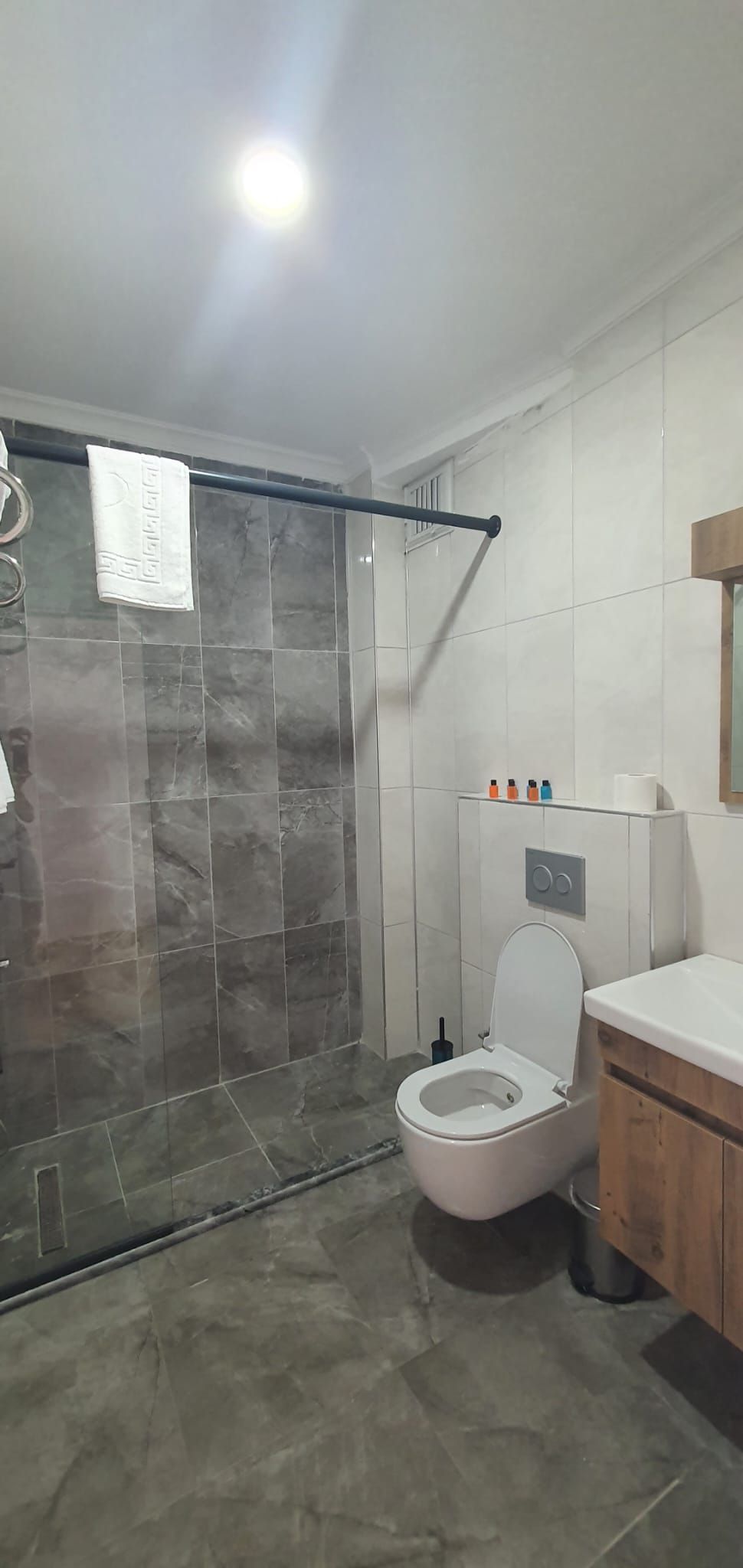 Ein modernes Badezimmer mit Duschkabine aus Glas, Toilette und Waschbecken mit Spiegel darüber.