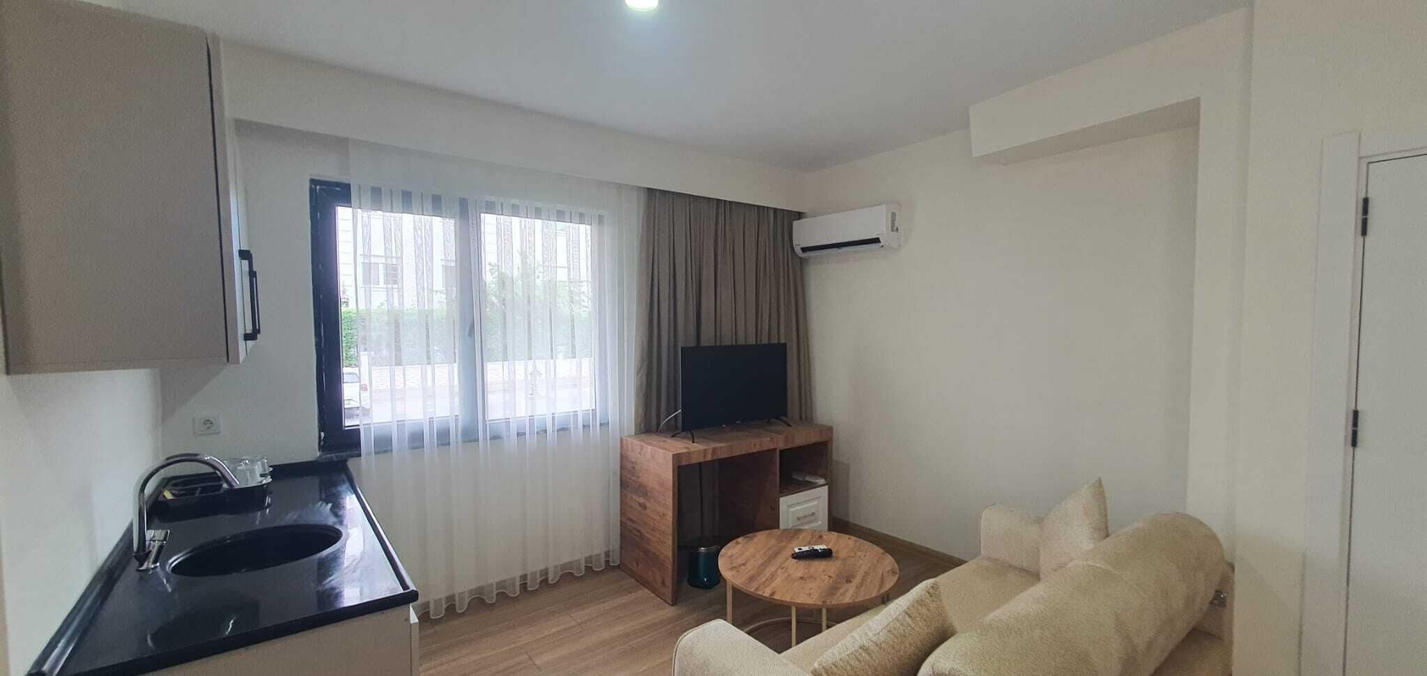 A compact living space with a kitchenette, a TV on a wooden stand, a sofa, and a small round table.