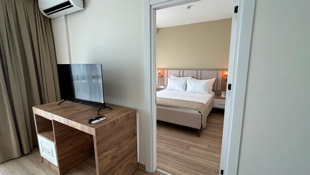 Una habitación de hotel con un escritorio de madera, un televisor de pantalla plana, una cama con ropa blanca y una mesita de noche con una lámpara.