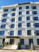Un hotel de varios pisos llamado "PETRA PORT" con una fachada simétrica, unidades de aire acondicionado y una entrada central con escalones.