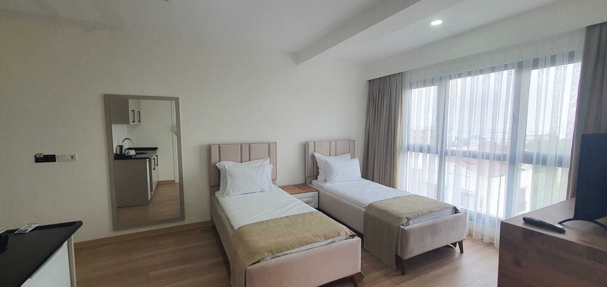A hotel room with two beds, a small kitchenette, and a balcony with curtains.