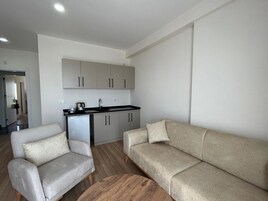 Una sala de estar moderna con un sofá y un sillón, una pequeña cocina y una mesa de centro de madera.