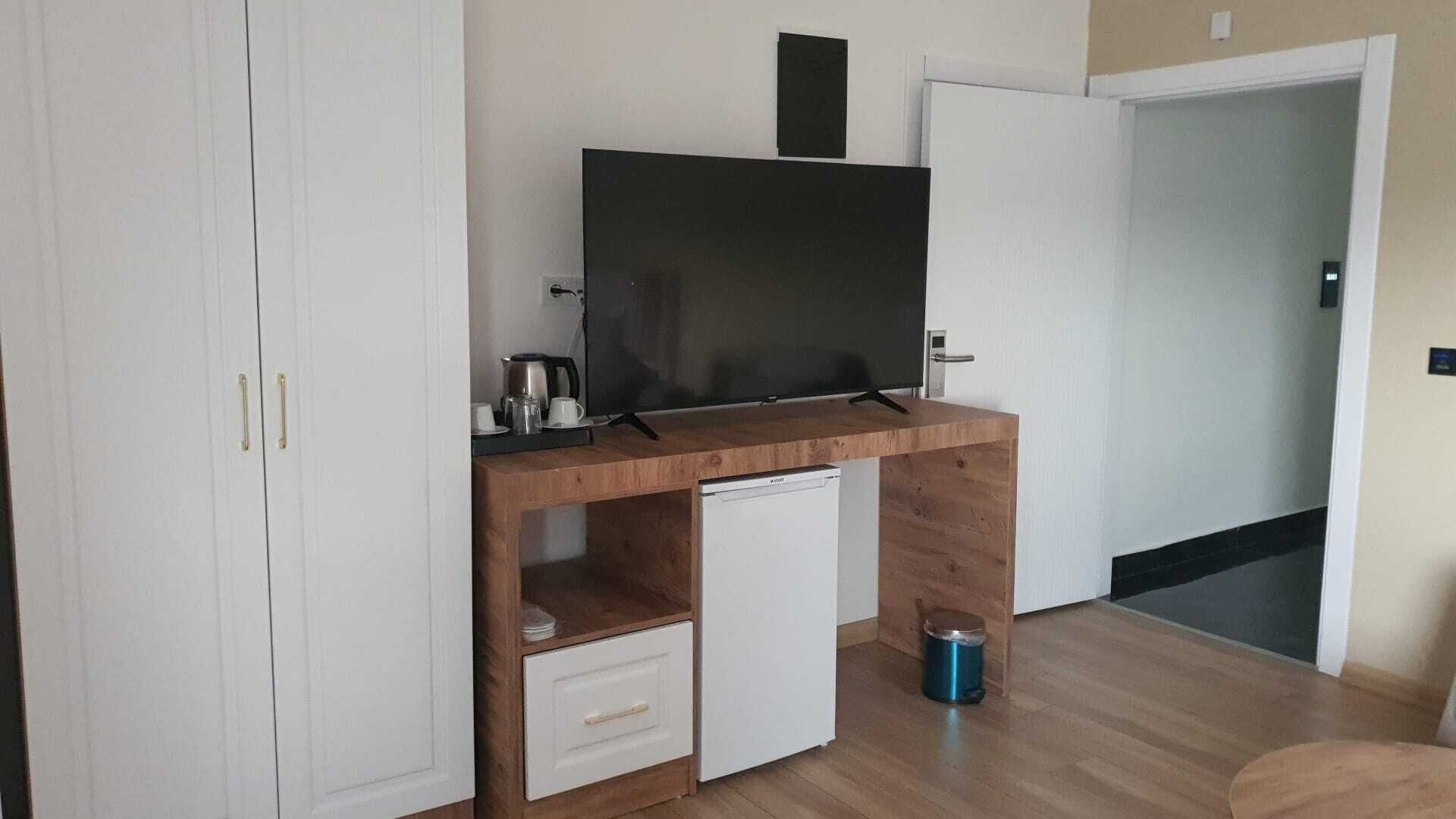Habitació compacta amb escriptori de fusta, nevera blanca petita, televisió i un armari amb calaix.