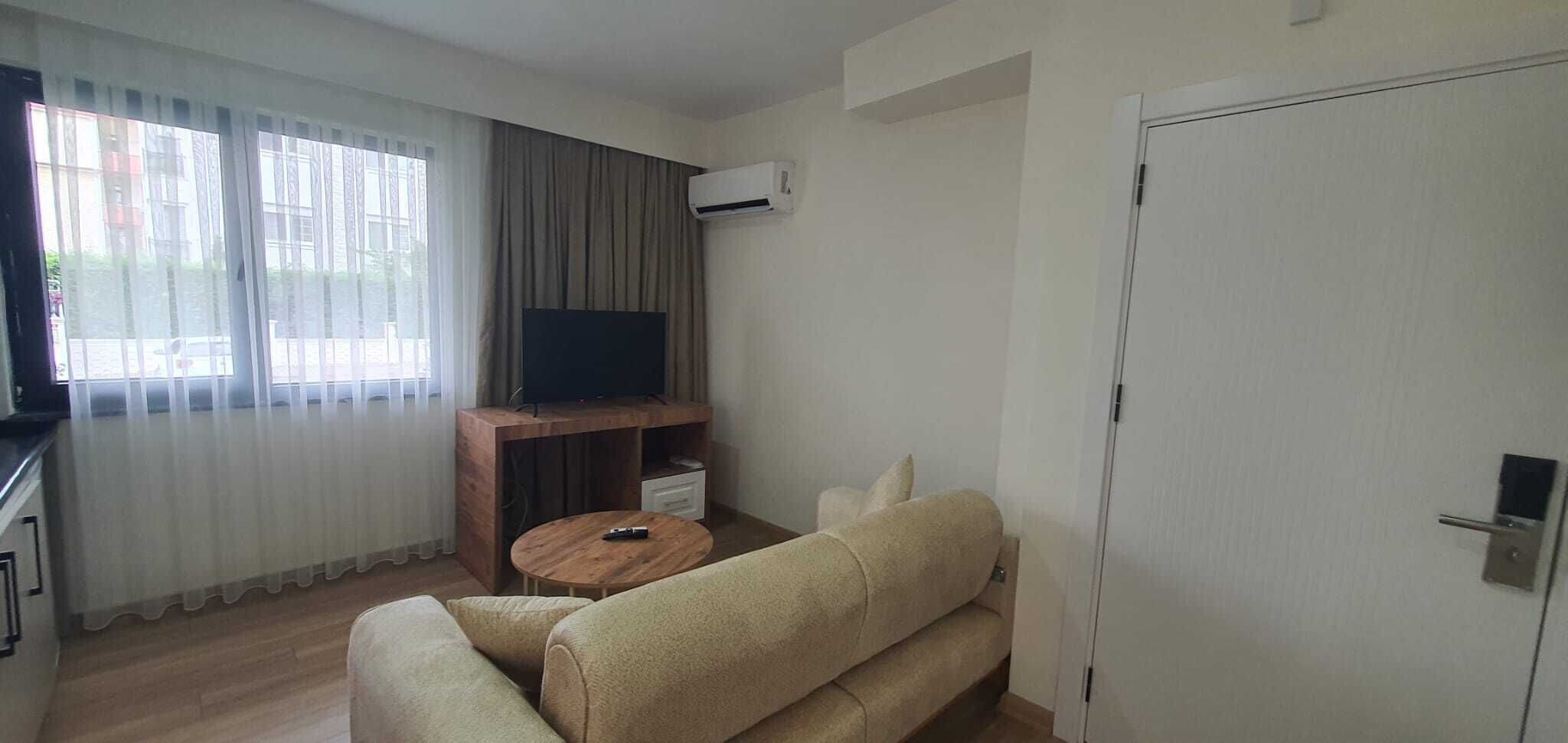 A living room with a sofa, a coffee table, a TV on a wooden stand, and a door.