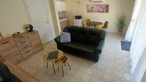 A living room with a sofa, a coffee table, a TV, and a dining area with chairs.