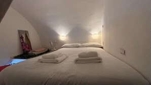 A cozy, dimly lit room with a large bed, two wall-mounted lights, and a statue on the wall. - Lola's House (Roma)