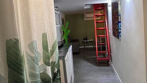 A narrow hallway with a kitchen area on the left, a red ladder, and a green plant. - Lola's House (Roma)