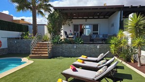 A poolside area with lounge chairs, a small pool, and a stone wall. - Casa Maracuya (Castillo Caleta de Fuste)