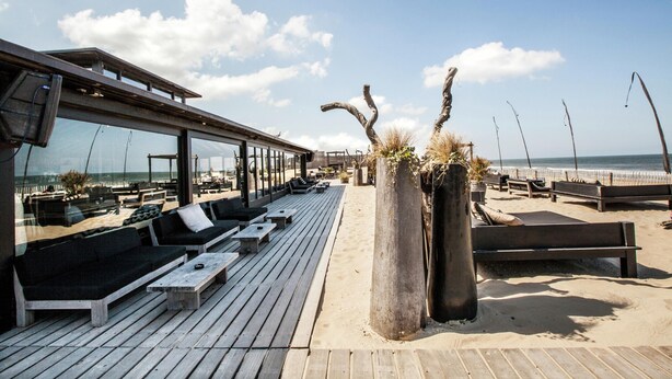 A beachside lounge with wooden deck seating and a glass-enclosed area overlooking the ocean. - Beach House in Zandvoort With Sea View (Zandvoort)