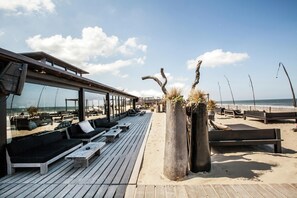A beachside lounge with wooden deck seating and a glass-enclosed area overlooking the ocean. - Beach House in Zandvoort With Sea View (Zandvoort)