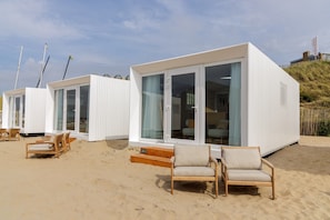 A beachfront property with modern white cabins, a sandy beach, and wooden beach chairs.