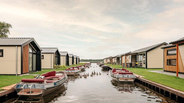 A canal with boats docked on either side, surrounded by modern buildings with large windows and flat roofs. - Nice and Cosy Chalet With ac and Sloop (Giethoorn)