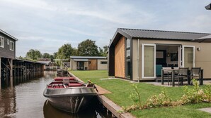 A modern house with a dock, a boat, and a grassy yard. - Nice and Cosy Chalet With ac and Sloop (Giethoorn)