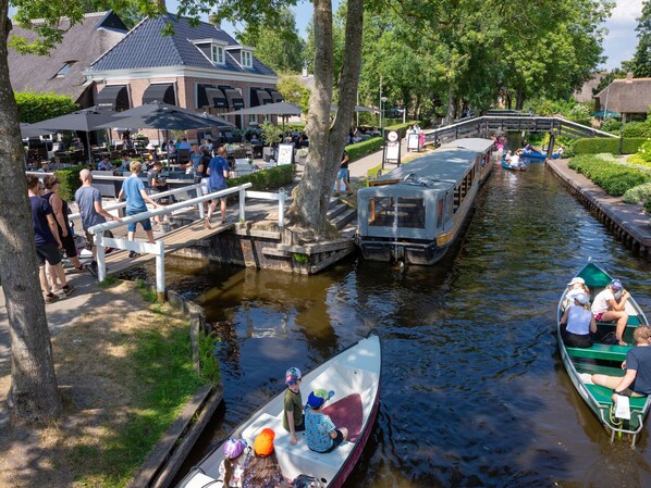 A riverside restaurant with outdoor seating, a bridge, and boats on the water. - Nice and Cosy Chalet With ac and Sloop (Giethoorn)