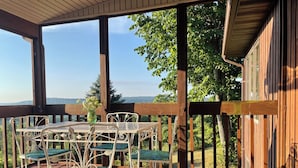 Un patio techado con cubierta de madera, mesa y sillas de metal, y vista a un área boscosa.