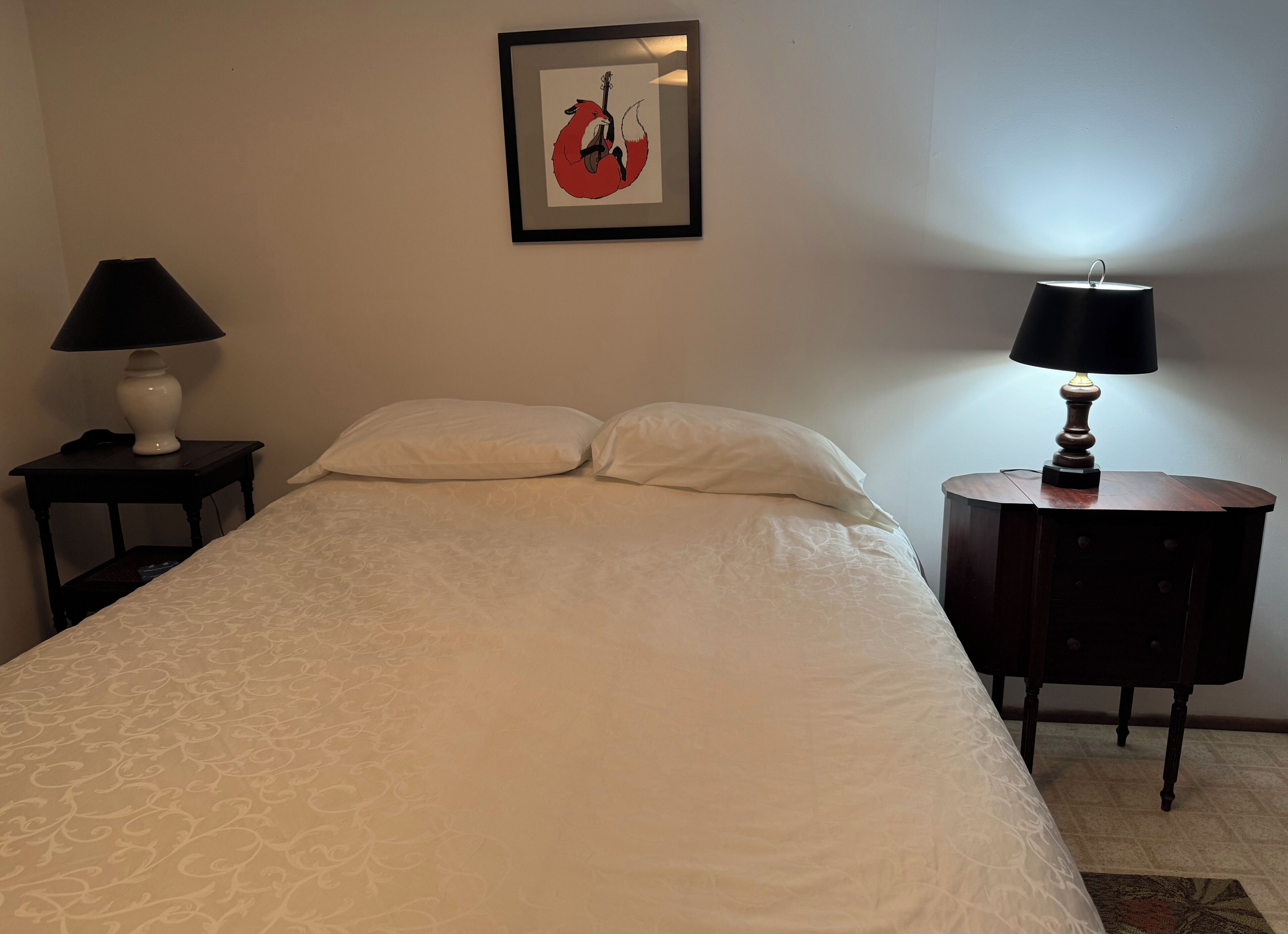 A neatly made bed with white linens, a framed artwork on the wall, and two bedside tables with lamps.