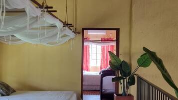 Habitación con dos camas, un tapete rojo, una planta en maceta y vista a una cortina y ventana rojas.