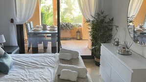 A bedroom with a bed, bedside table, dresser, and a view of the outdoor patio. - Luxury complex 2 bed apartment with 5 pools and close to beaches, marina & golf (MANILVA)