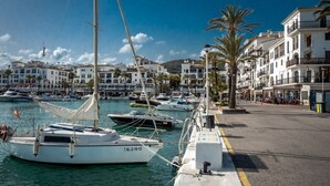 A marina with several sailboats docked, a waterfront promenade with buildings, and a clear blue sky. - Luxury complex 2 bed apartment with 5 pools and close to beaches, marina & golf (MANILVA)