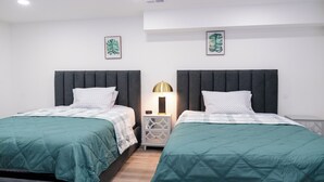 Ein Hotelzimmer mit zwei Betten, jeweils mit dunkelbrauner Kopfteil und türkisblau gewählter Bettwäsche. Dazwischen steht ein Nachttisch mit einer Lampe.
