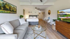 A modern living room with a sofa, a glass coffee table, a TV, and a ceiling fan. - Remodeled Ground floor studio, AC, across from the beach, close to everything (Kihei)