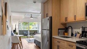 A compact kitchen with wooden cabinets, a refrigerator, a microwave, and a dining area with a table and chairs. - Remodeled Ground floor studio, AC, across from the beach, close to everything (Kihei)
