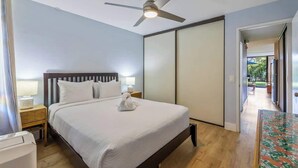 Un dormitorio con cama, mesitas de noche, ventilador de techo y vistas al exterior.