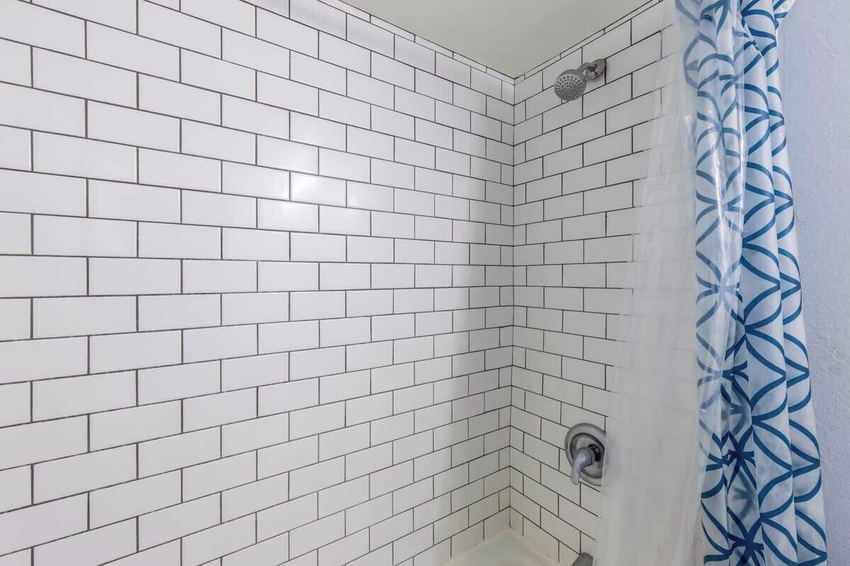 A corner shower with white tiled walls and a showerhead.