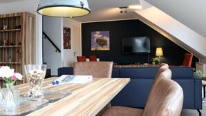 A modern living room with a wooden dining table, a large pendant light, a TV mounted on the wall, and a blue sofa. - Nice Apartment With Dishwasher, in a Residence 500 m. From the ski Lift (Winterberg)