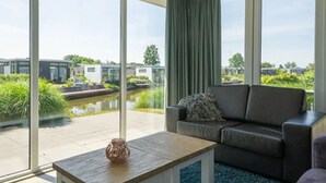 A modern living room with a large window, a sofa, a coffee table, and a view of a canal and buildings. - Chalet on the Water at the Beautiful Veluwemeer (Nunspeet)