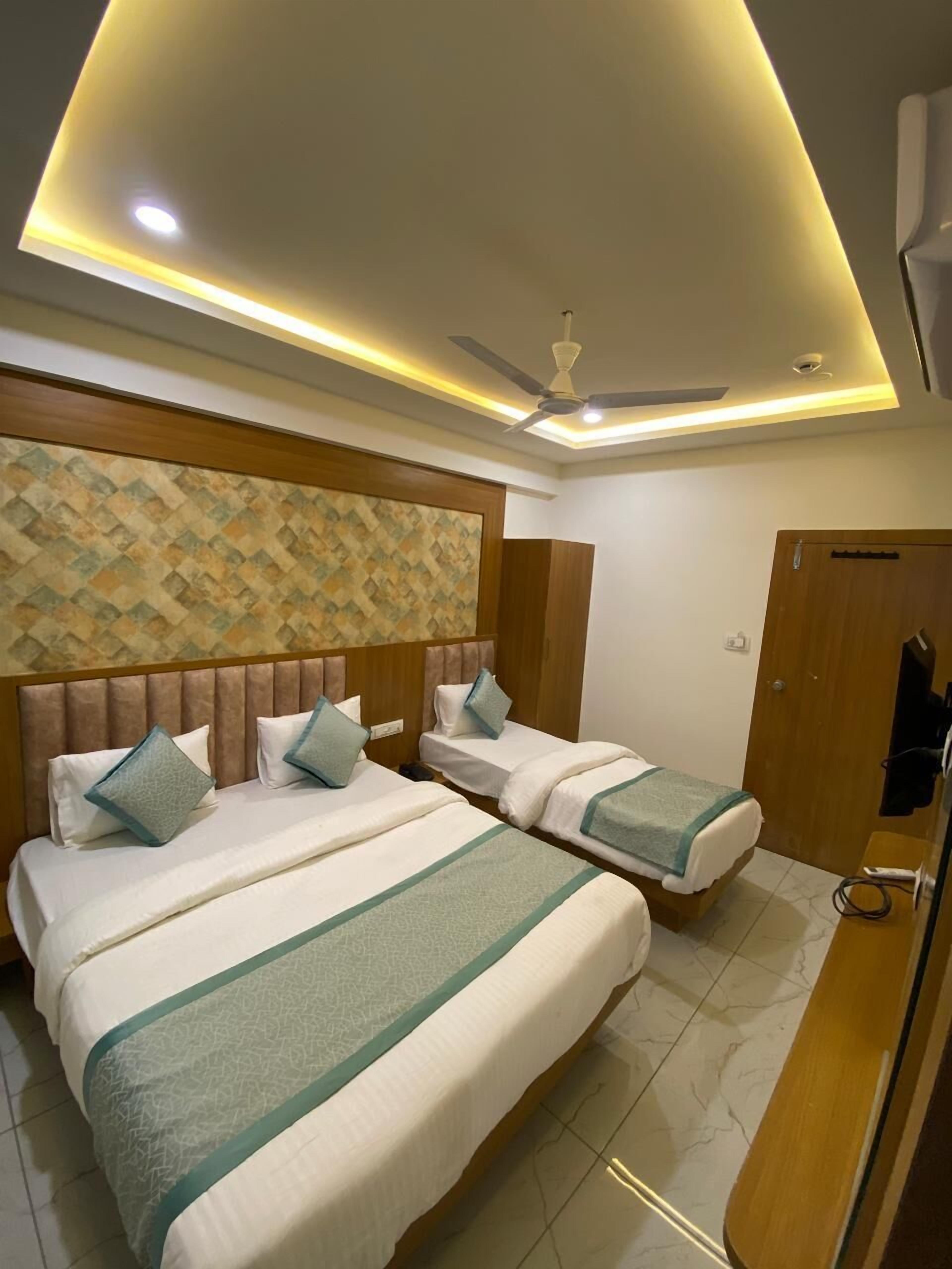 A hotel room with two beds, a ceiling fan, recessed lighting, a patterned wall, and a wooden wardrobe.