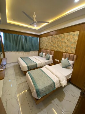A hotel room with two beds, a ceiling fan, a desk, and a window with curtains. - Hotel Neptune (Ahmedabad)