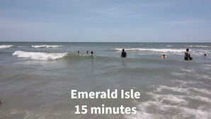 Une scène de plage avec des personnes dans l’eau, des vagues et un texte indiquant « Emerald Isle, à 15 minutes ».