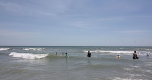 En strandscene med mennesker i vandet, bølger og tekst der viser 'Emerald Isle 15 minutter'.