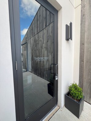 Enter 'THE APARTMENT' through the large glass door with a sleek metallic handle.