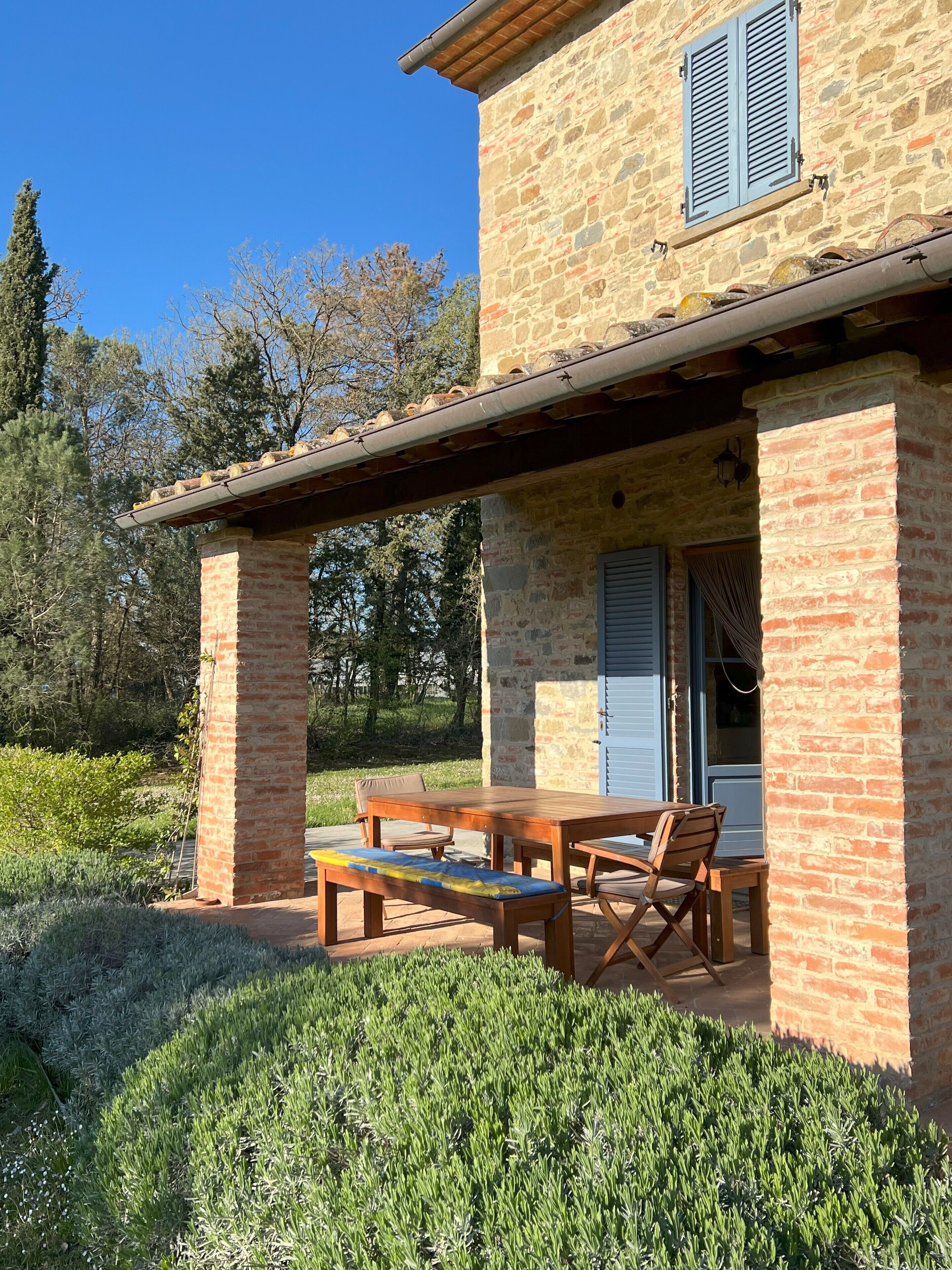 A stone building with a covered patio, outdoor seating, and a door with shutters.