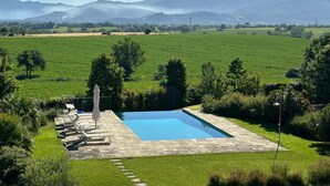Une piscine rectangulaire bordée de pierres, entourée d’une pelouse bien entretenue et d’arbres.