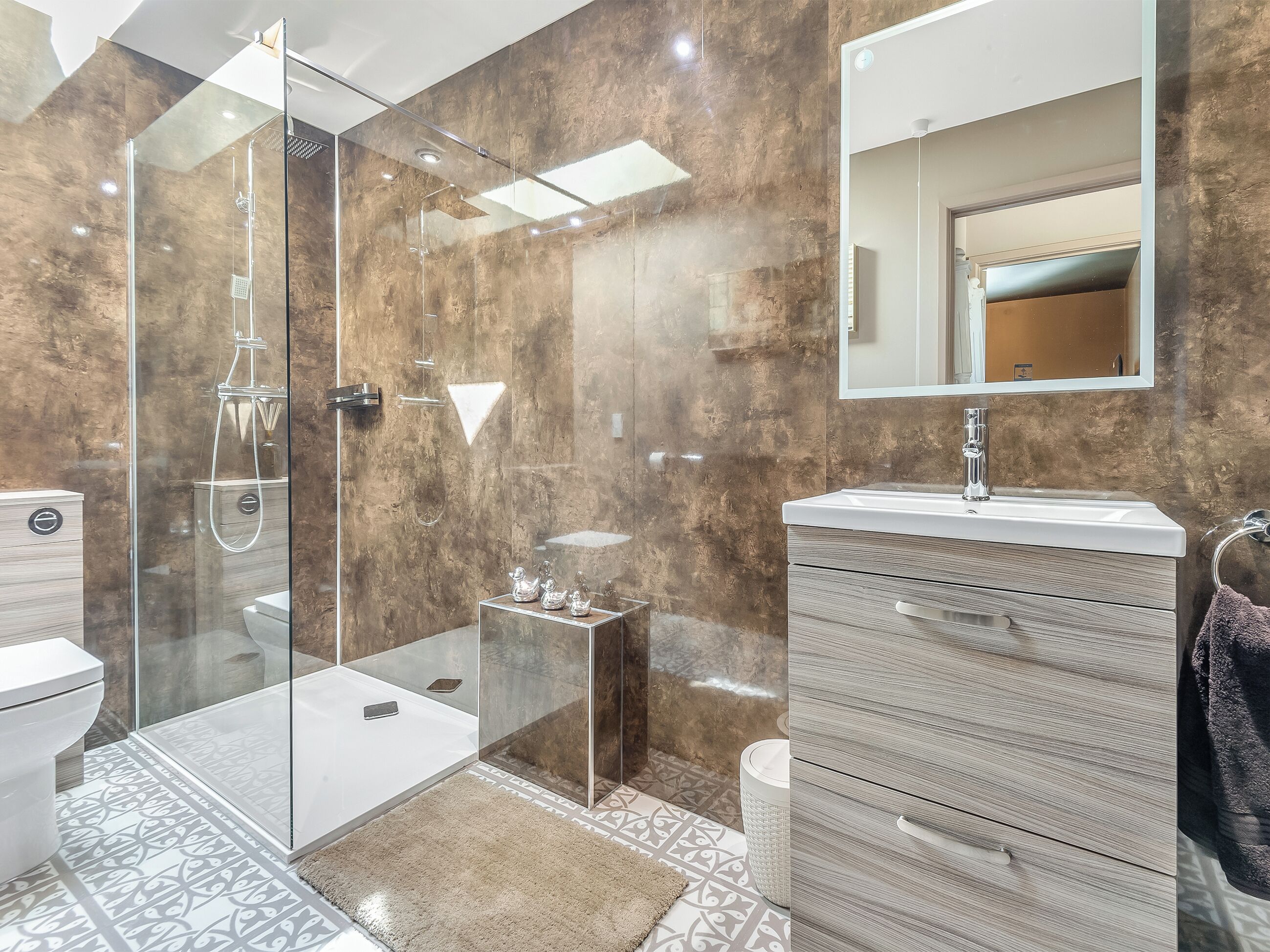 A modern bathroom with a glass-enclosed shower, a vanity with a mirror, and patterned tiles.