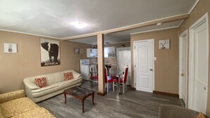 Una sala de estar con sofá, una mesa de centro de vidrio y un comedor con sillas rojas. Se ve una cocina al fondo, con un refrigerador y un microondas.