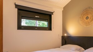 Ein Hotelzimmer mit zwei Betten, einem Fenster mit Blick auf Bäume, einer Wandleuchte und einer Steckdose.