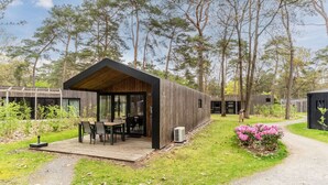 Ein modernes Blockhaus mit Holzterrasse, Essbereich und Blick auf den umliegenden Wald.