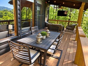 Une terrasse extérieure avec une table en bois, des chaises et un téléviseur fixé au mur.