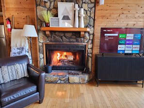 A cozy living room with a stone fireplace, a leather sofa, and a flat-screen TV displaying streaming services.
