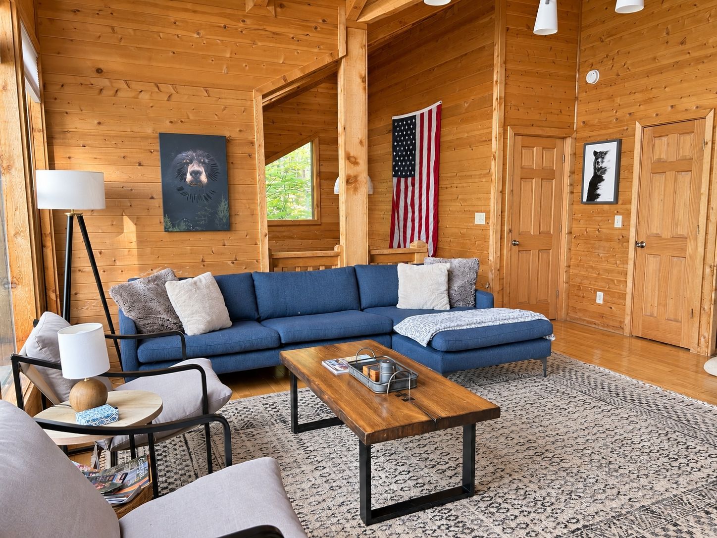 A cozy cabin interior with a blue sectional sofa, a wooden coffee table, and a patterned rug.