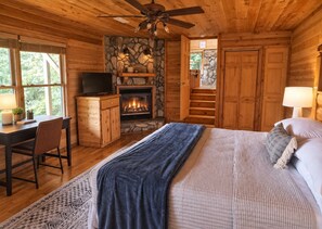 Une chambre située dans une cabane en rondins, avec une cheminée, un lit, un bureau avec une chaise et un téléviseur.