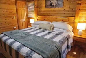 A wooden cabin-style room with a bed, a nightstand with a lamp, and a wooden door. - Family Mountain Retreat - Hot Tub, Games & Views (Blue Ridge)