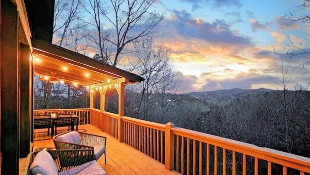 Eine Holzterrasse mit Sitzgelegenheiten und Lichterketten mit Blick auf eine gebirgige Landschaft.